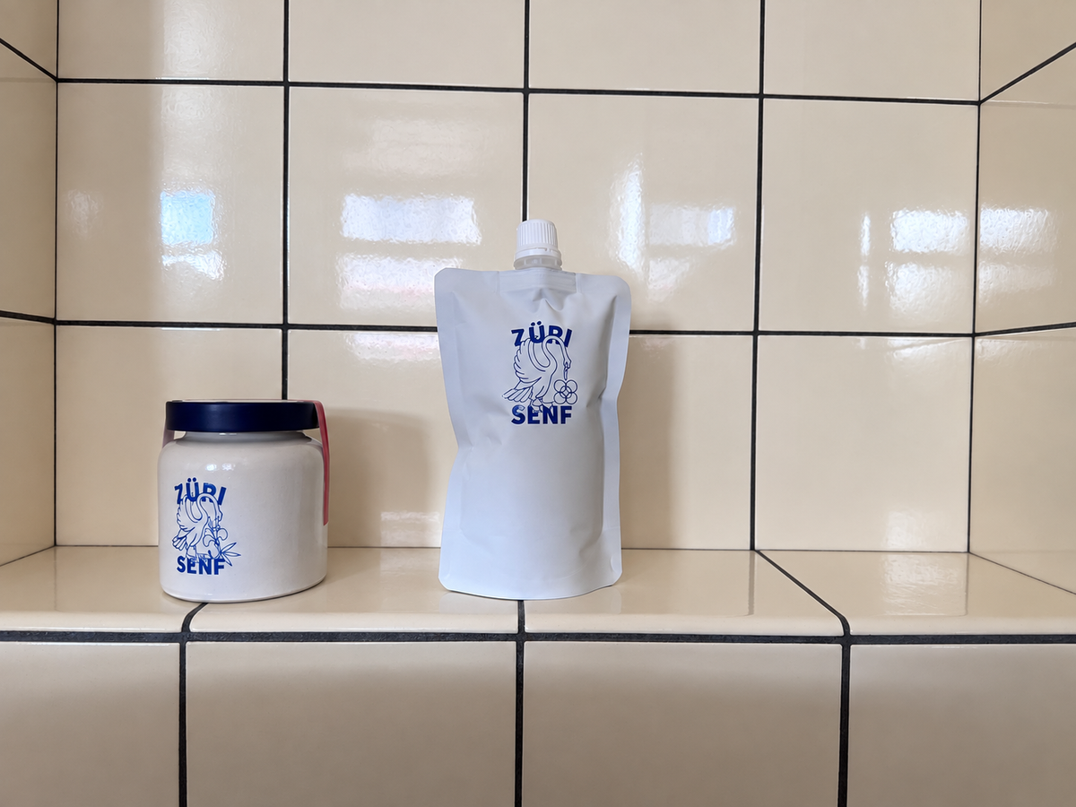 ZÜRI SENF Steinguttöpfli und Quetschbeutel vor einer gefliesten Wand